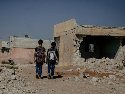 In Idlib, Syria, two students walk along an unpaved road through the ruins of a city devastated by war