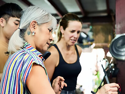 A senior woman teaches tourists how to prepare traditional Thai dishes in a warm and lively kitchen