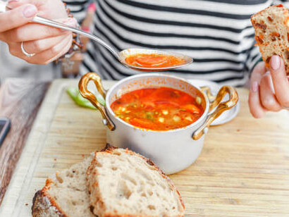 A woman enjoys traditional Hungarian goulash soup from a pot at an outdoor restaurant