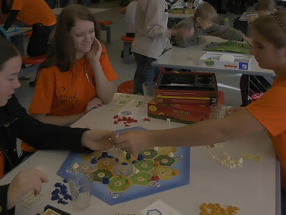 Strategic gaming unfolds as young girls enthusiastically dive into the Settlers of Catan board game, illustrating the captivating experience offered by this popular game