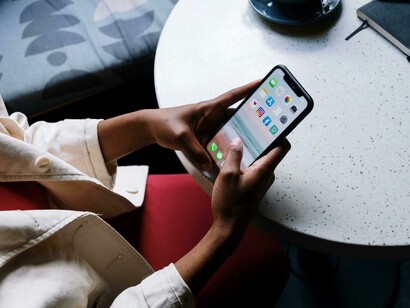 A person sits at a café table, checking social media on a black iPhone