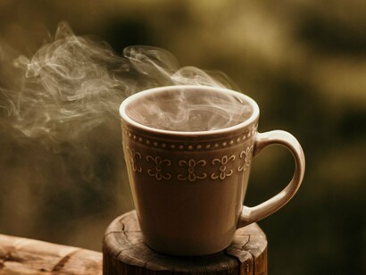 O vapor sobe de uma caneca de café apoiada sobre uma superfície de madeira, em uma cena marcada pela simplicidade. A lembrança do cafezinho preparado por He-Man na Tribuna de Imprensa transforma um gesto cotidiano em uma memória de amizade e companheirismo