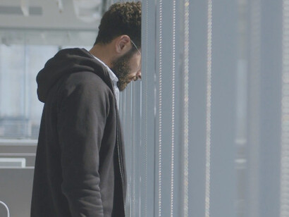 From behind the office window, he watches the world move on, silently struggling within the walls of his own workplace