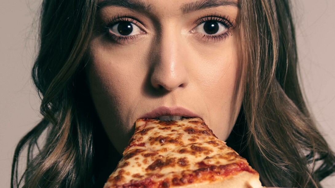 A woman looks shocked as she takes a bite of a slice of pizza