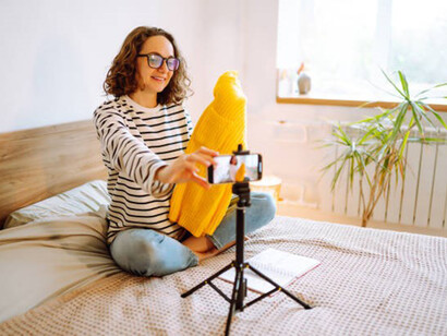 Beautiful fashion blogger holding yellow sweater dreamily recording new fashion video for vlog
