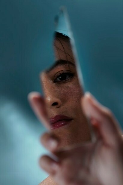 A woman holds a broken mirror in her hands, its jagged edges reflecting fragmented images of her face, symbolizing introspection and the complexity of self-perception