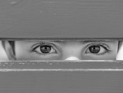 The vacant gaze of a child standing behind what resembles a wooden frame