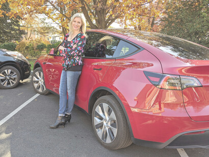 A blonde woman leans on the door of her red EV