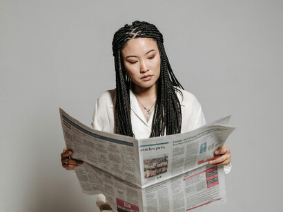 A woman with braided hair sits quietly, reading a newspaper