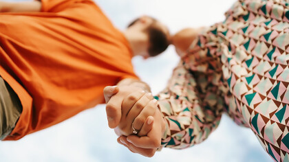 Joyful young couple dressed in vibrant clothing, posing against a bright sky backdrop