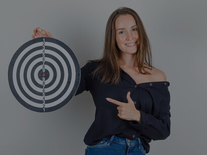 A young woman in a black shirt marking a dartboard, illustrating the precision and intent of setting actionable goals and creating a detailed action plan