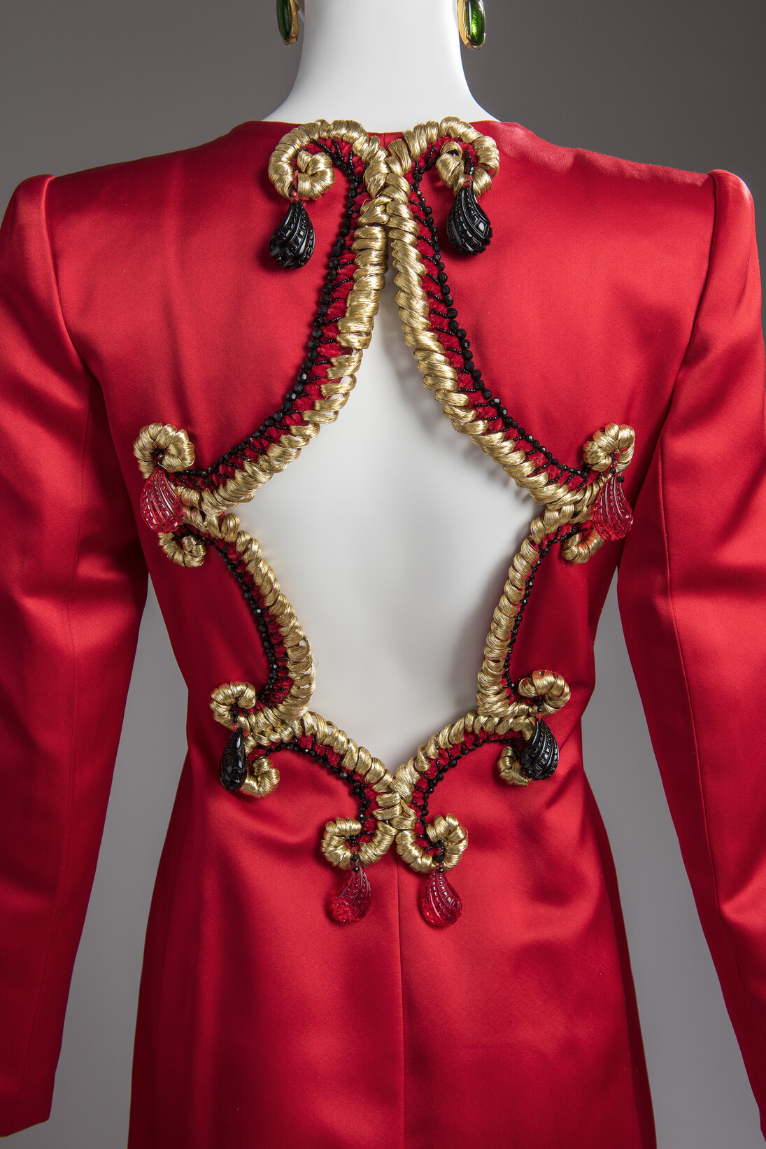 Abrigo-vestido de noche en satén rojo rubí, abierto por la espalda y ribeteado con hilo dorado y colgantes rojos y negros. 1975 / Maison Givenchy. Foto: Luc Castel con la colaboracion de Philippe Caron