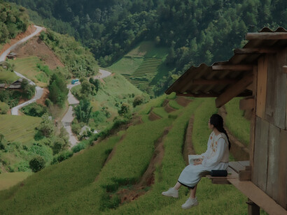 Set amidst layers of lush agricultural fields, a quaint hut serves as an emblem of sustainable farming. On its porch, a woman sits, personifying the principles of clean and responsible food production