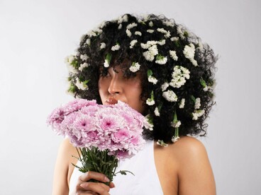 A woman peering over a bouquet of soft pink blooms, representing the quiet journey from self-consciousness toward self-awareness