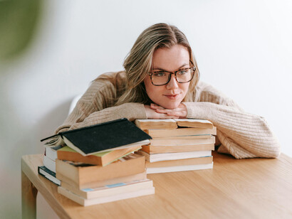 A young woman reading a book beside a heap of literature