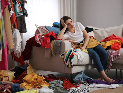 Upset young woman with lots of clothes on sofa in room