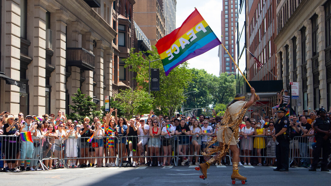 Membro da comunidade LGBTQIAPN+ corre com bandeira escrito Paz na parada da diversidade de Nova Iorque nos Estados Unidos da América