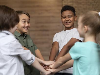 Bambini in cerchio con le mani in centro una sopra all'altra: "La soluzione a questo problema si trova nell’apprendimento cooperativo, ovvero creando dei contesti in cui la cooperazione tra i vari gruppi etnici diventa essenziale per il bene di entrambi"