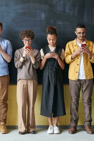 A group of people stands near a blackboard, each focused on their phones instead of the board