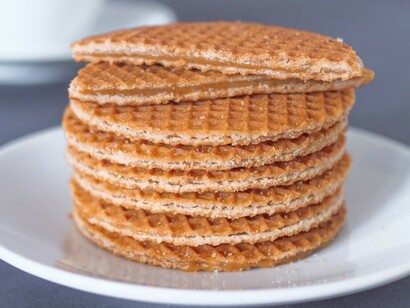 A white ceramic mug alongside stroopwafels served on a matching white ceramic plate