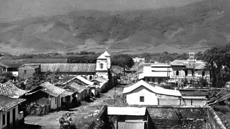 Cartago, Costa Rica, 1902, vista de norte a sur. Detalle de imagen captada por el fotógrafo estadounidense Benjamin Lloyd Singley (1864-1938). Al centro, a la izquierda, la vieja iglesia del Carmen y, en frente, calle en medio, el mercado. Al centro (derecha), el chalet de Rafael Ángel Troyo, en construcción. Al sur de la iglesia, los frondosos higuerones del parque central; a lo lejos, el antiguo matadero, inaugurado en 1887 (donde hoy está la plaza Asís). Colección Biblioteca del Congreso, EE. UU.
