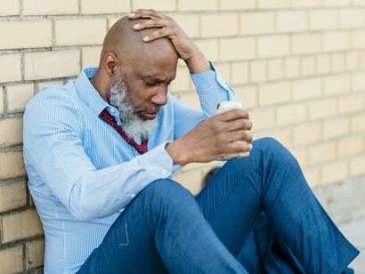 A weary worker holding his head in frustration beside a city wall, reflecting the growing mental exhaustion of ordinary citizens