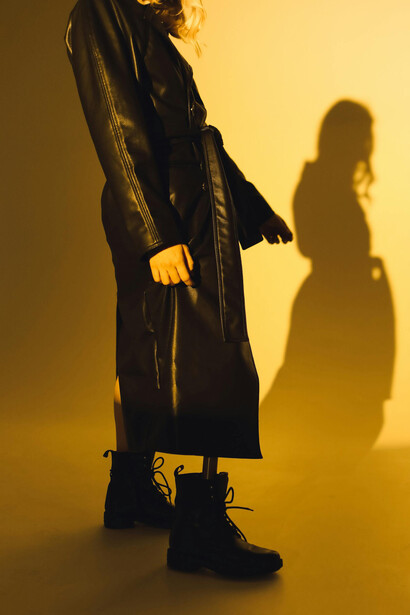 Modella in trench di pelle nero su set fotografico di sfondo giallo