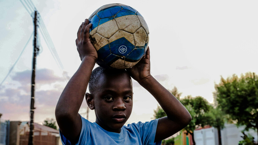 Criança brinca com bola de futebol na rua do bairro enquanto pratica a inspiração por seus ídolos do gramado