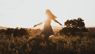 Mujer pasea por una pradera durante la puesta del sol