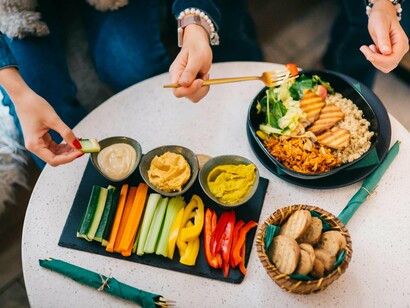 Na foto aparece as mãos de duas pessoas comendo alimentos feitos a partir de produtos de origem vegetal