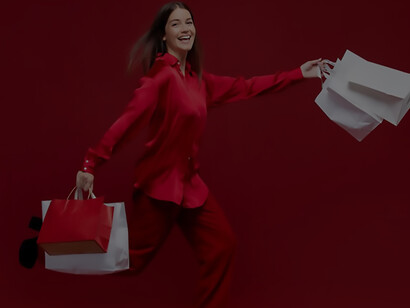 A delighted woman stands, holding a collection of vibrant shopping bags with a cheerful smile on her face