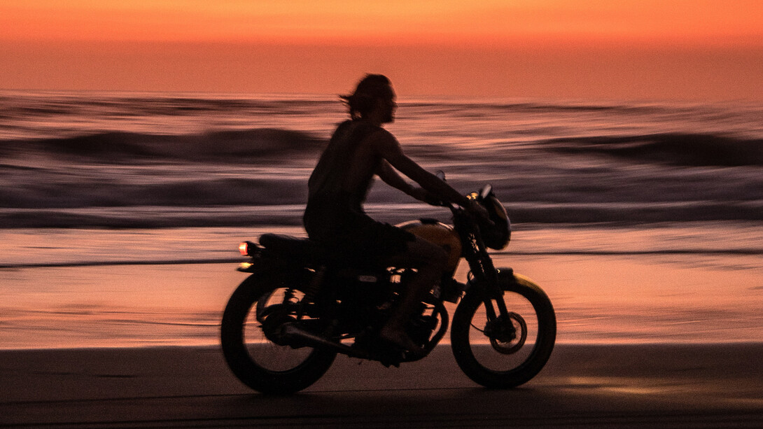 Homem pilota moto em areia da praia próximo ao mar