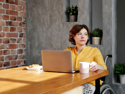 A woman wearing a yellow long-sleeve shirt works on her laptop while seated in a black wheelchair