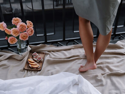A white bed set up on the balcony, with pink roses and a woman next to it