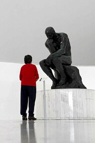 A young man looking at The Thinker statue by Auguste Rodin in a museum and wondering, what is man?