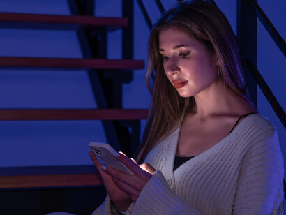 A young woman on the stairs, absorbed in her smartphone under blue evening light, illustrating digital addiction
