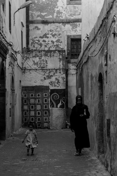 In the heart of Essaouira, Morocco, a woman and her child explore streets steeped in history, where diverse traditions converge in a celebration of tolerance and unity