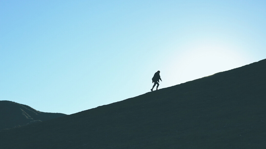 Mujer caminando cuesta arriba hacia la cima de una montaña. Para este 2023, haz que tus sueños vuelen, incluso más allá de lo que visualizas