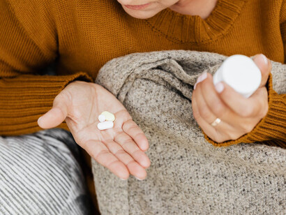 Persona con pillole in una mano e flaconcino di medicinali nell'altra