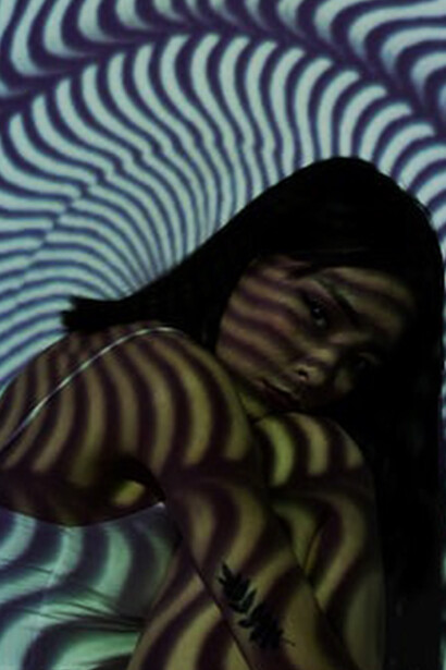 The woman with a contemplative air sat in the room, her reflection casting a connection to the abstract art gracing the background