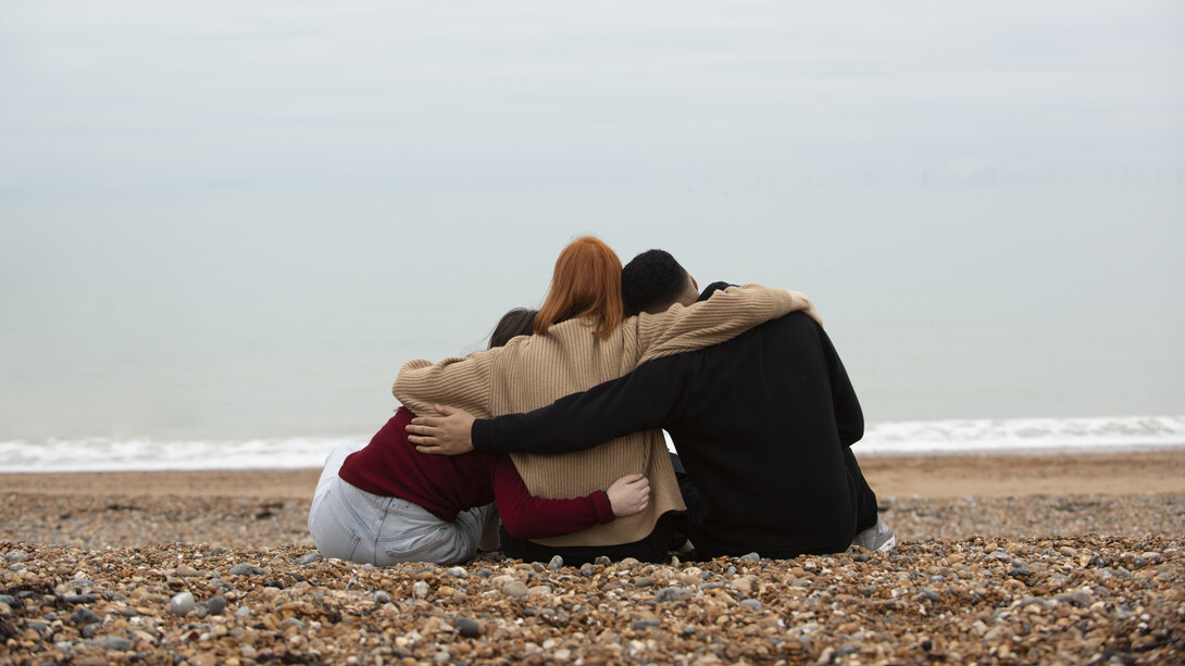 Un moment de connexion avec trois personnes se serrant dans les bras sur la plage, capturant la beauté des instants simples et authentiques