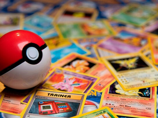 A Poké Ball resting among scattered vintage trading cards, representing the transformation of childhood hobbies into valuable collectibles
