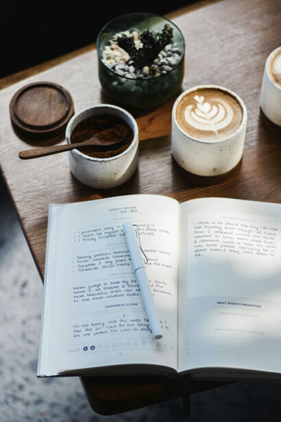 Una mesa acogedora con un café, un cuaderno y una lapicera. Tener siempre en cuenta que con frío, hambre y poca luz es muy difícil escribir