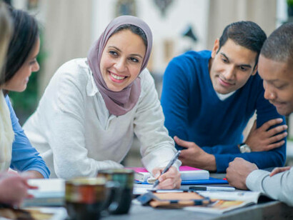 A multicultural team of young entrepreneurs, with one migrant wearing a turban, gathers around a table to discuss their business ideas