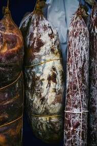 Hanging cured meats, suspended in a rustic and artful display, evoke an air of culinary craftsmanship and timeless tradition