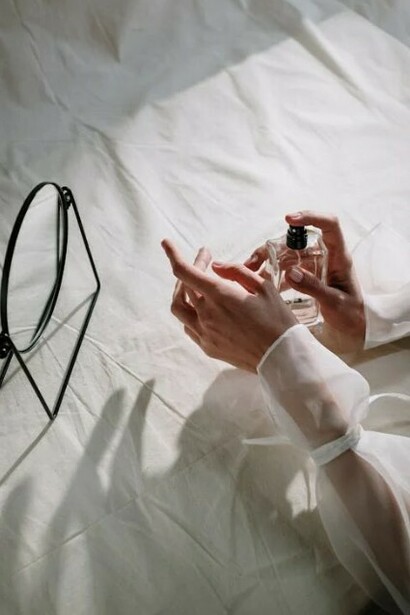Resting her arm on white sheets, a woman puts perfume on her wrist