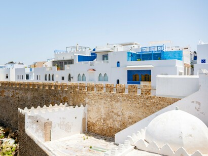 Whitewashed buildings with vivid blue details rising behind historic stone walls in Asilah, Morocco, representing the character of Morocco’s coastal communities