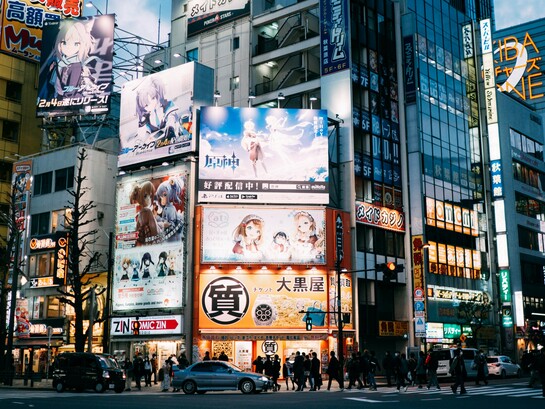 A bustling Tokyo district surrounded by towering anime billboards and media advertisements, symbolising the cultural prominence anime and manga have achieved in Japan and beyond