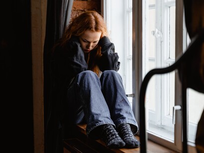 A woman sat on a windowsill with her hands on her head. Journaling can provide insight into inner thoughts 