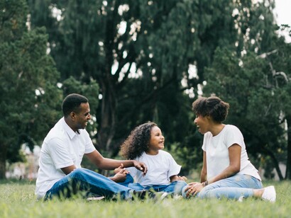 A family of three sitting down on the grass in the park